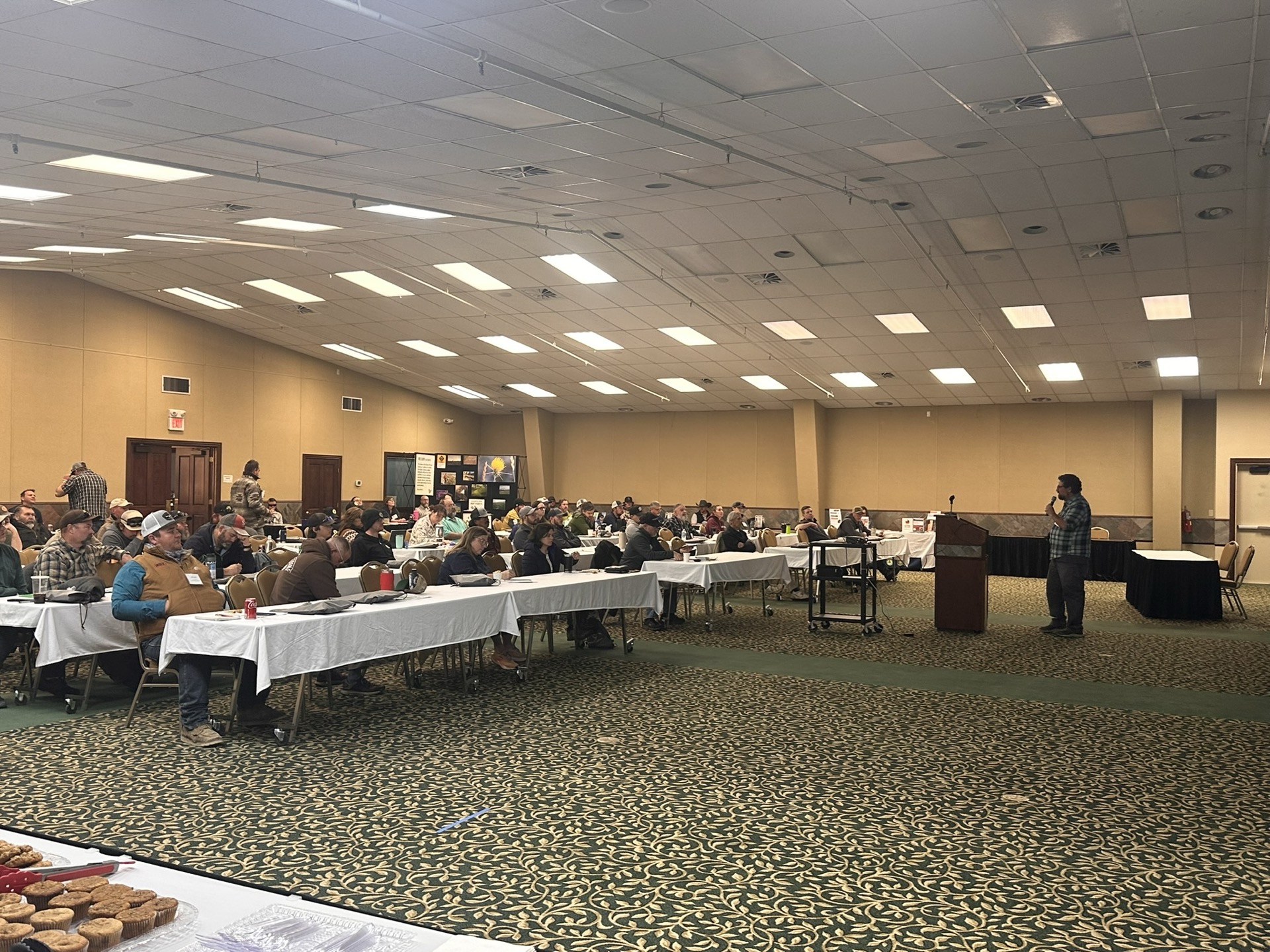 ENLC's Invasive Species Conference in session, with attendees seated at long tables and a presenter at the podium